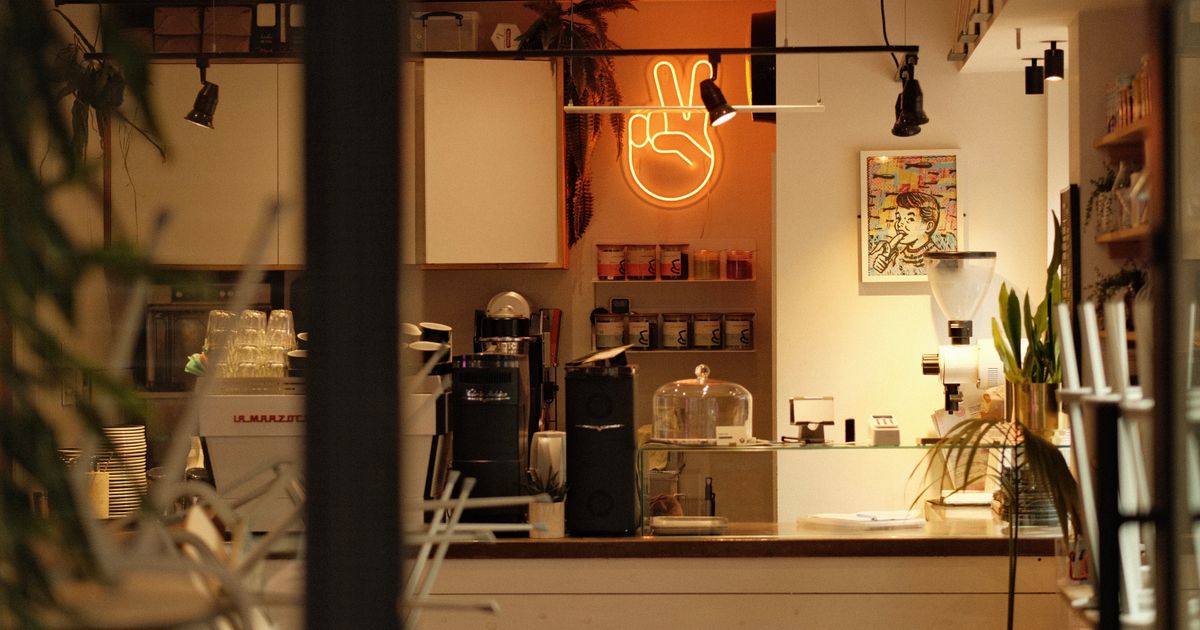A small cafe counter lit up and ready, seen from the street through the window, with nobody inside.
