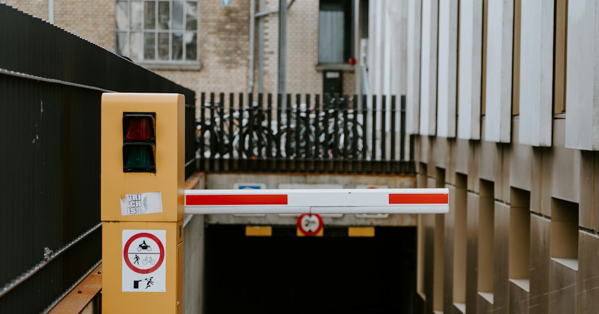 A red and white barrier arm lowered across the entrance to an underground car park, with a red light showing.