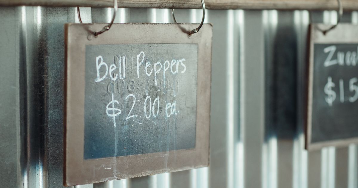 A chalkboard sign hanging on a metal wall that reads "Bell Peppers $2.00 ea."