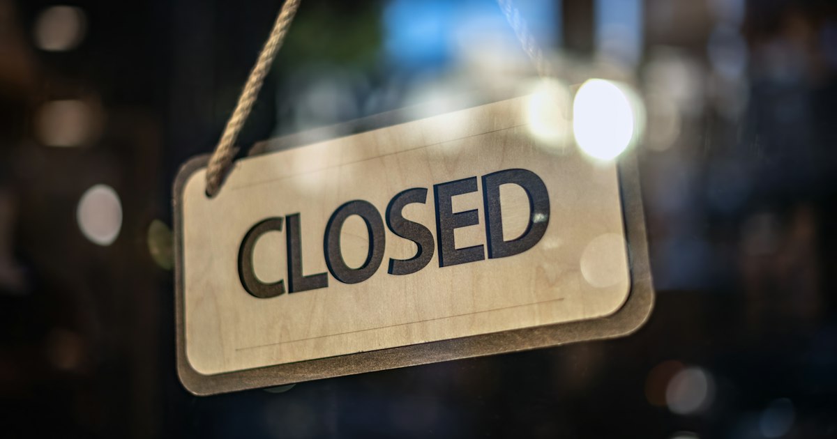 A wooden CLOSED sign hanging on a rope inside a shop window.