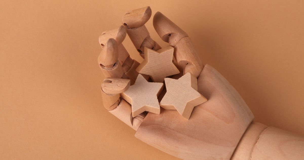 A wooden artist's mannequin hand clutching three wooden star shapes against a terracotta background.