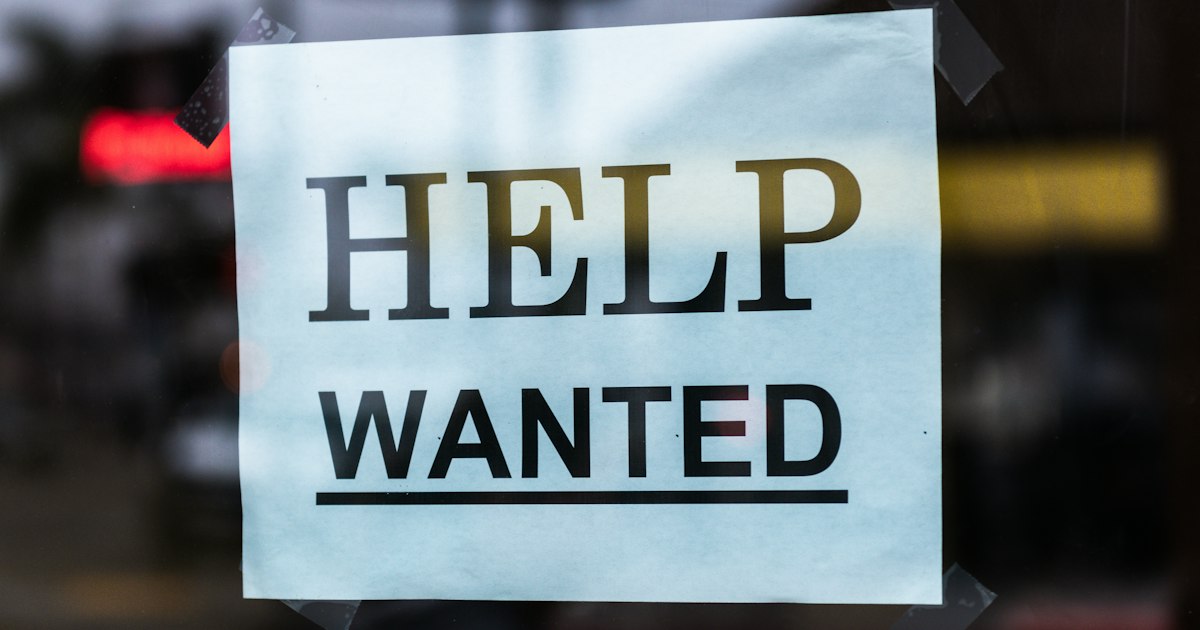 A printed HELP WANTED sign taped to the inside of a shop window.