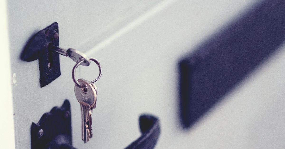 A bunch of keys left hanging in the lock of a front door that has not been locked.