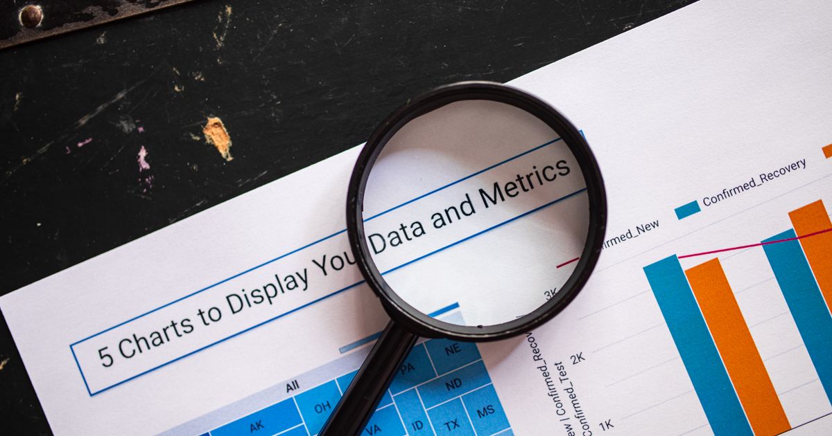 A magnifying glass resting on a printed page of bar charts and data tables.