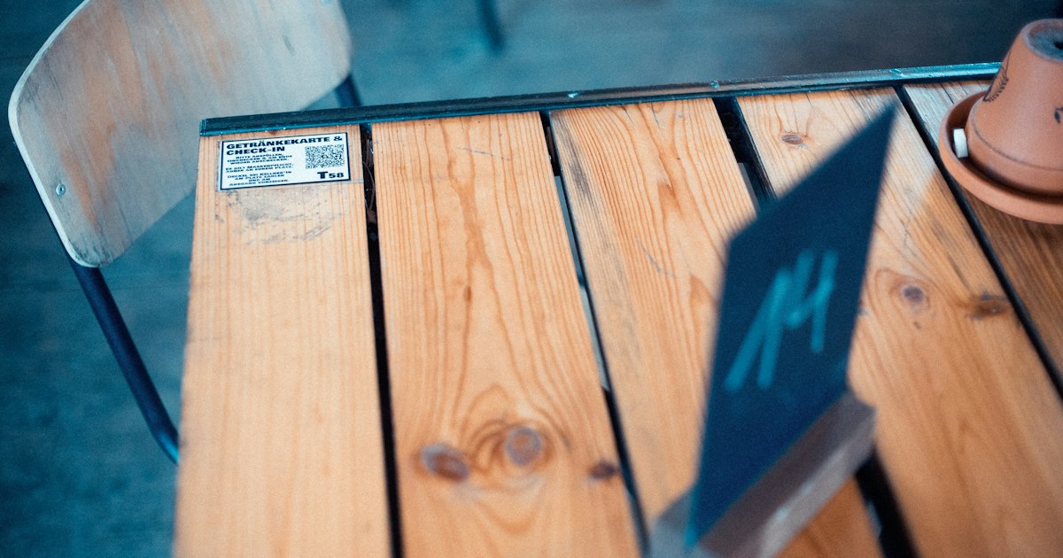 A small QR code sticker for a drinks menu stuck to the corner of a wooden café table.