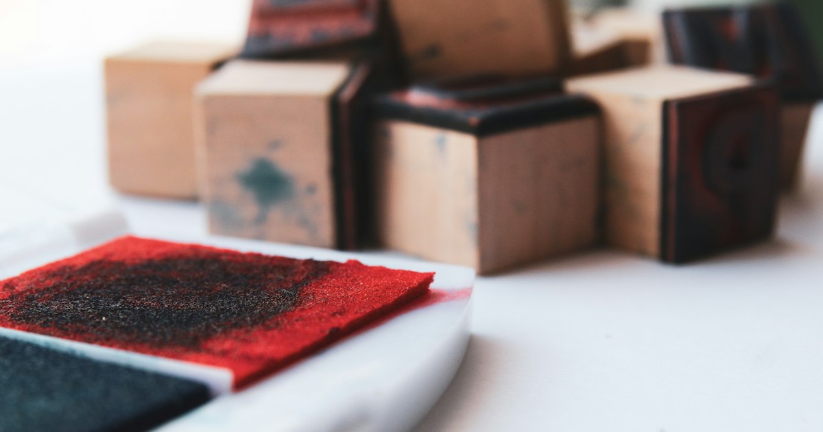 Wooden rubber stamps beside a red and black ink pad on a white surface.