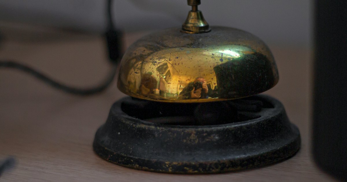 A worn brass service bell on a wooden counter, with nobody attending the desk.